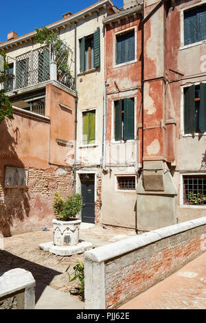 Venice court with ancient water well, buildings and houses facades in a sunny day in Italy Stock Photo