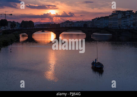 Ponte alla Carraia spans the River Arno in the city of Florence. Here the dramatic sky, reflection and stillness at sunset is captured. Stock Photo