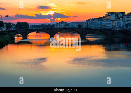 Ponte alla Carraia spans the River Arno in the city of Florence. Here the dramatic sky, reflection and stillness at sunset is captured. Stock Photo