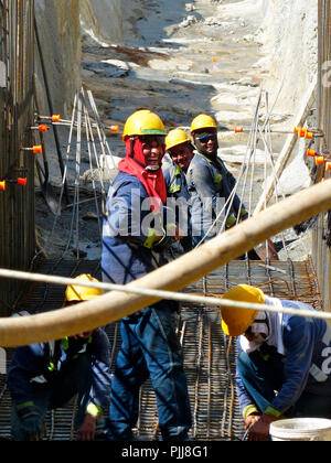 a group of five welders building the mesh for a concrete reinforcement in a hydropower Project wearing safety helmets and smiling Stock Photo