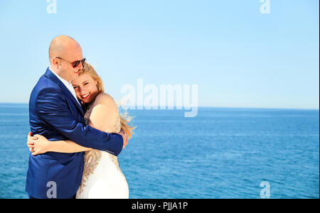 Wedding. Happy couple day wedding. Beautiful bride and groom at the beach. Cheerful married couple standing and smiling by the sea. Wedding couple. Stock Photo