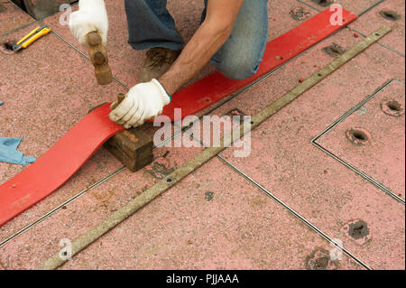 Worker wearing gloves, punching holes in leather strap, with hammer and punch tool. Stock Photo