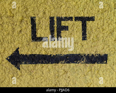 Word 'LIFT' and arrow painted in black on yellow wall pointing at the direction of the lift / elevator Stock Photo