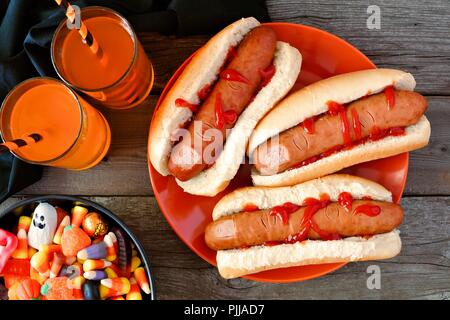 Halloween meal scene with hot dog fingers, drinks and candy, above view a wood background Stock Photo