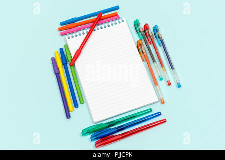 Spiral bound lined notepad surrounded by different coloured pens Stock Photo