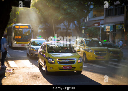 RIO DE JANEIRO - CIRCA MARCH, 2018: Taxis and buses drive along a busy tree-lined street in Ipanema with the sun setting behind and sea mist Stock Photo