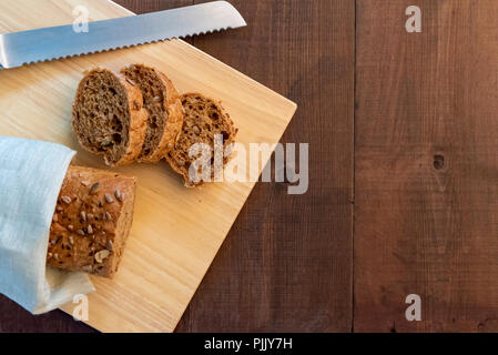 Whole seeded baton or baguette with bread knife on a wooden board. Stock Photo