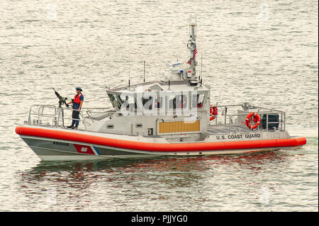 U.S. Coast Guard boat - a member of the US Coast Guard mans a gun on his escort boat for a cruise ship in Boston harbor USA - Boston Massachusetts Stock Photo