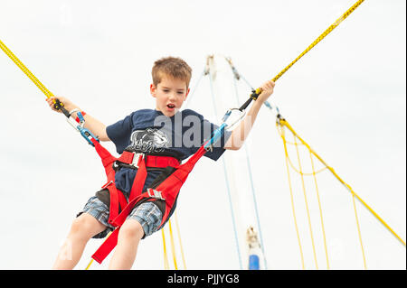 Bungee jump trampoline boy - an excited young boy practices bungee jumping in a harness - cruise ship activities / activity Stock Photo