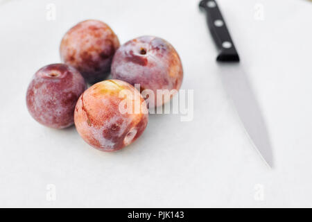 A knife beside four honey punch pluot fruits on white wax paper Stock Photo