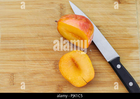 An amigo pluot chopped in half atop a wood cutting board Stock Photo
