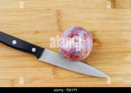 One fresh Honey Punch Pluot on a wood chopping board with a knife Stock Photo