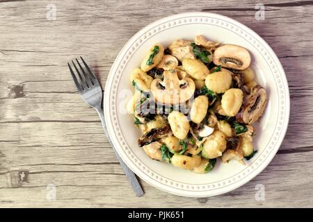 Gnocchi with a mushroom cream sauce, spinach, chicken and sun dried tomatoes, top view on a wood background Stock Photo