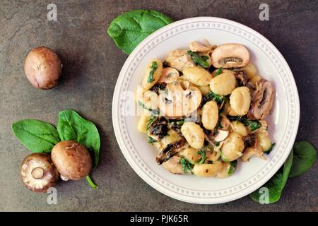 Gnocchi with a mushroom cream sauce, spinach, chicken and sun dried tomatoes, top view on a dark stone background Stock Photo
