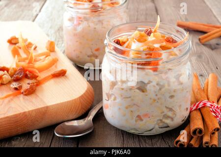 Carrot cake overnight oats with nuts and raisins in mason jars, still life on a rustic wood background Stock Photo