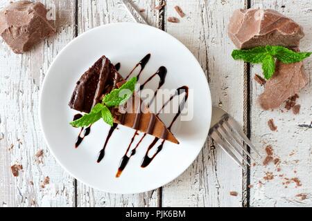 Slice of chocolate cheesecake on plate, above view over a rustic white wood background Stock Photo