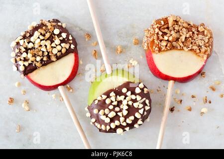 Three autumn apple lollipops dipped with chocolate and caramel, overhead view on marble Stock Photo