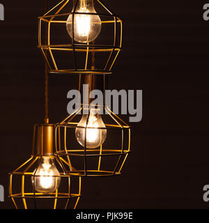 Ceiling chandelier with hanging three bulb lamps, yellow LED lighting elements covered with metal wire frame lampshades, square framed photo with sele Stock Photo
