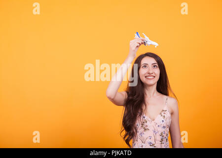 Young beautiful woman playing with toy plane in studio over yellow background. Ready to go traveling Stock Photo