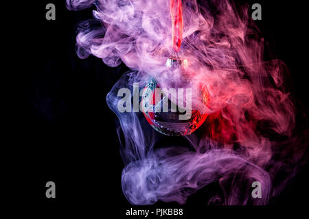 Close up  of a  red shiny decoration Christmas balls in colored purple-red smoke, on an isolated black background. Concept of a modern Christmas card. Stock Photo