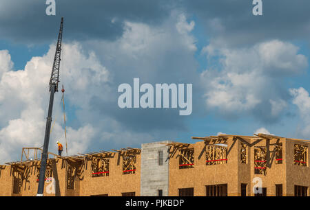 Construction workers on roof with crane and cumulus clouds in background Stock Photo