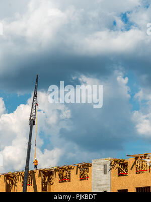 Construction workers on roof with crane and cumulus clouds in background Stock Photo