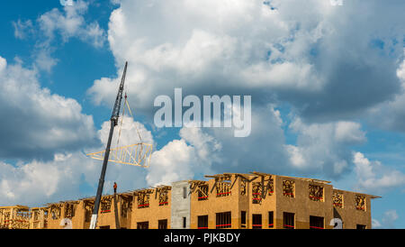 Construction workers on roof with crane and cumulus clouds in background Stock Photo