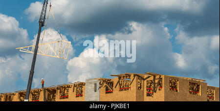 Construction workers on roof with crane and cumulus clouds in background Stock Photo