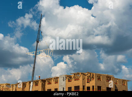 Construction workers on roof with crane and cumulus clouds in background Stock Photo