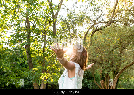 Young woman meditating and embracing her beautiful life  standing with her arms outspread as the rising sun touches her face in a woodland setting, up Stock Photo