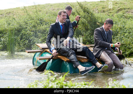 Three wearing black suits getting wet from a hose pipe on a raft in a river at The Lowland Games, Thorney, Somerset, England Stock Photo