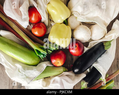 vegetables in eco cotton bags on table in the kitchen, zero waste shopping. flat lay. mushrooms, zucchini,eggplant, pepper, tomato, nectarines on wood Stock Photo