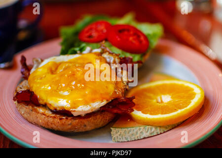 Breakfast toasted bagel bun served with bacon, sausage and egg sandwich with fruits. Stock Photo