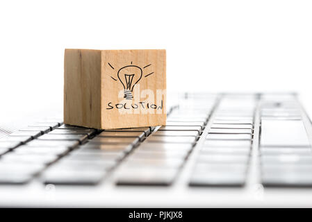 Innovation concept with the word Solution and a hand-drawn illuminated light bulb on a wooden block lying on a computer keyboard, copyspace on white b Stock Photo