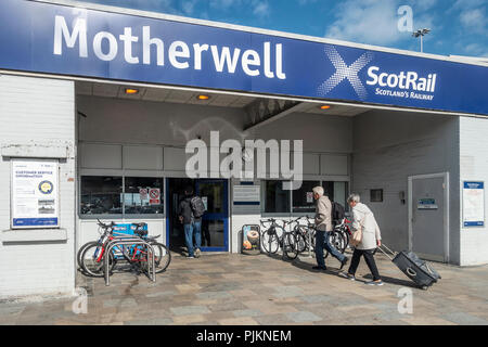 Passengers entering Motherwell ScotRail railway station. Two men with rucksacks, one woman pulling a suitcase on wheels. Bicycle racks. North Lanarksh