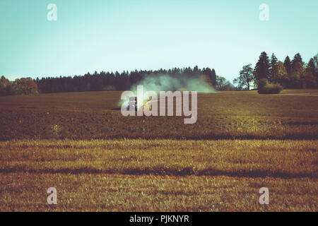 A tractor with a trailer driving at high speed through the landscape and pulling a cloud of dust behind, Stock Photo