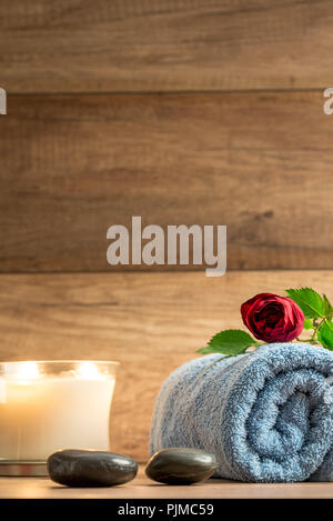 Romantic wellness arrangement with a burning candle, red petals, two massage stones and a rose on a blue folded towel. Stock Photo