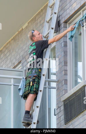Male washes windows on an apartment complex while standing on a ladder. Stock Photo