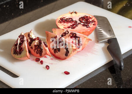 Cut pomegranate isolated on cutting board with knife Stock Photo