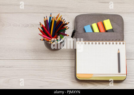 School supplies. Metal stand for pencils with color pencils, open exercise book on bag-pencil case with color felt pens and marker on grey wooden boar Stock Photo