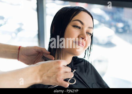 Happy young woman getting a new haircut by hairdresser at parlor Stock Photo