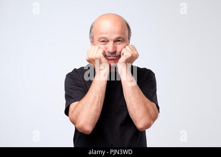 Gloomy bald european male model showing boredom while leaning head on hand and standing over gray background. Stock Photo