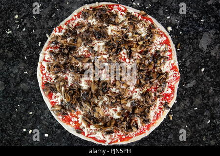 Pizza with mushrooms on black table, ready to be put in the oven to be baked Stock Photo