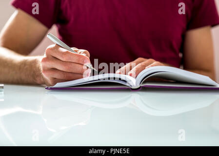 Close up of a Student Writing Notes or Homework on a Clean Notebook on Top of White Table. Stock Photo