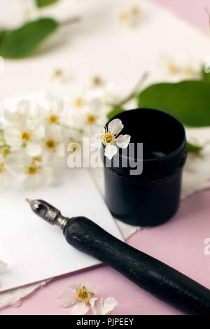 Envelope, paper, white flowers, black ink and fountain pen. Styled feminine desk workspace with white flowers, calligraphy nib, ink, envelope and whit Stock Photo