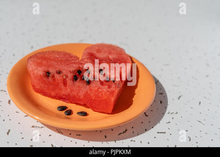 Heart made of watermelon on the orange plate and white background with small black texture Stock Photo