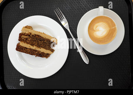 Overhead view of a cup of frothy milky coffee with heart shaped design, fork, chocolate walnut cake on black background in London UK  KATHY DEWITT Stock Photo