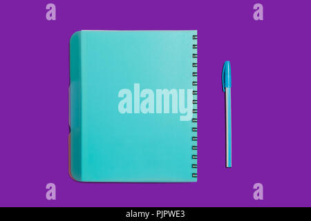 Blue spiral notebook lying near a pen on a purple background. concept of office stationary. free copyspace Stock Photo