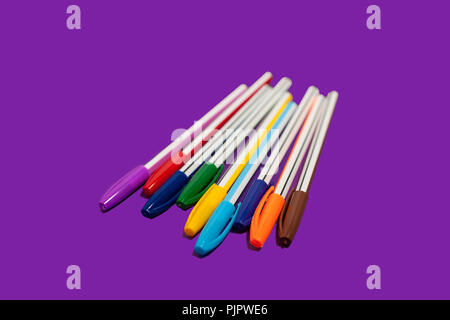 different new bright colored pens lying on a purple background. concept of office supplies Stock Photo