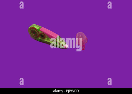 plastic colored opened tape corrector lying near its cap on a purple background isolated. concept of office chancery Stock Photo